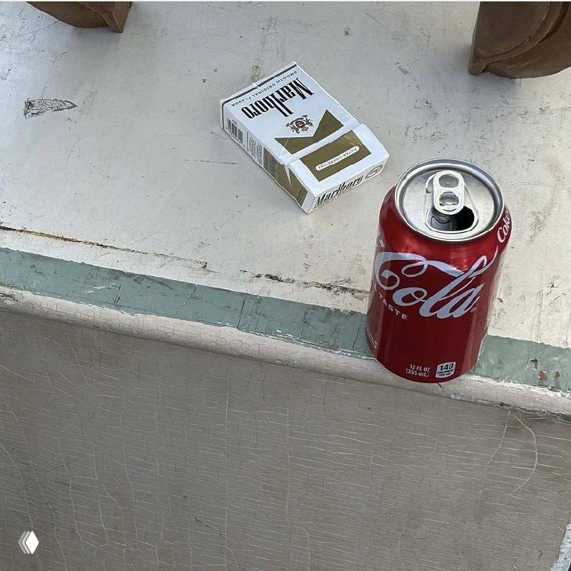 Пачка сигарет рядом с открытой банкой Coca‑Cola на подоконнике; потертая поверхность и винтажная атмосфера создают урбанистическую эстетику.