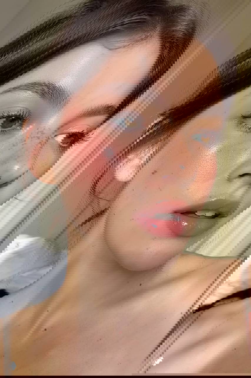 Портрет молодой женщины с яркими розовыми румянами на щеках, легкими веснушками и глянцевыми губами в дневном свете.