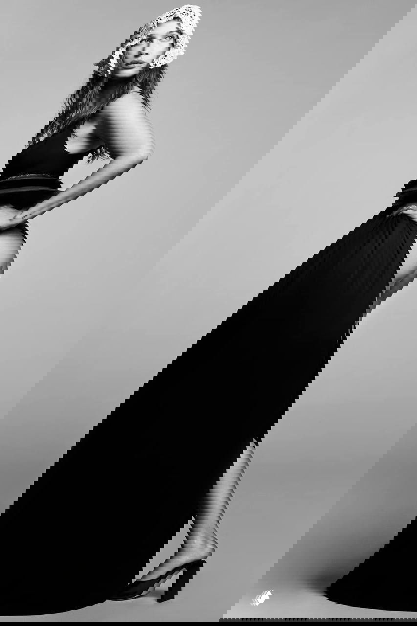 Чёрно‑белая студийная фотография женщины в длинной юбке с боковой деталью, поза в полоборота, выдержанный модный редакционный стиль.