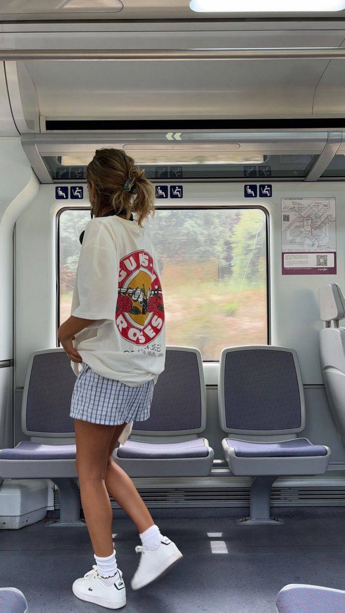 Девушка в свободной футболке и клетчатых шортах в салоне поезда, вид из окна и расслабленный летний образ в дороге.