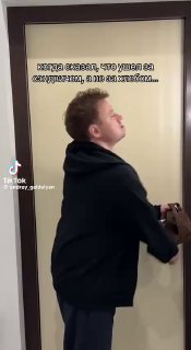 Вертикальный кадр из видео: мужчина в тёмной толстовке поворачивается к двери; видны подписи и водяной знак платформы, динамичный ракурс.