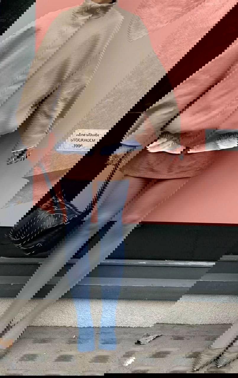 Стрит-лук у витрины: женщина в пастельных голубовато-серых колготках, мини-юбке и бежевой куртке — спокойная цветовая гамма и минимализм.