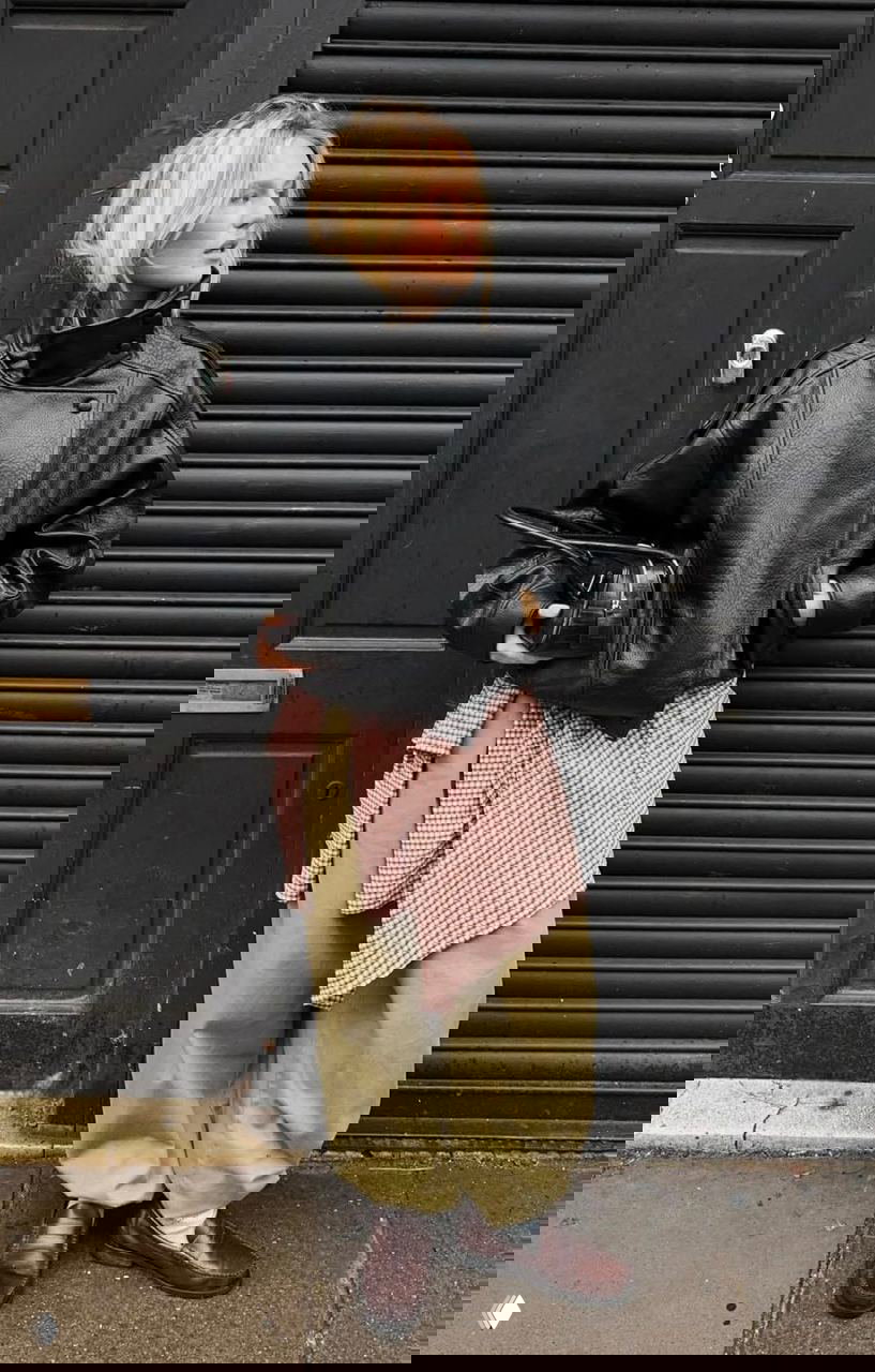 Уличный образ: девушка в чёрной кожаной куртке с выраженным высоким воротником-стойкой, широкие брюки и массивные лоферы в городской стилистике.