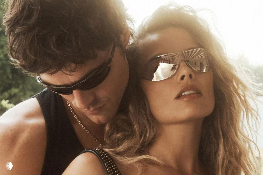 Крупный план Марго Робби в солнцезащитных очках и Джейкоба Элорди рядом; настроение летнего ретро и сексуальной притягательности.