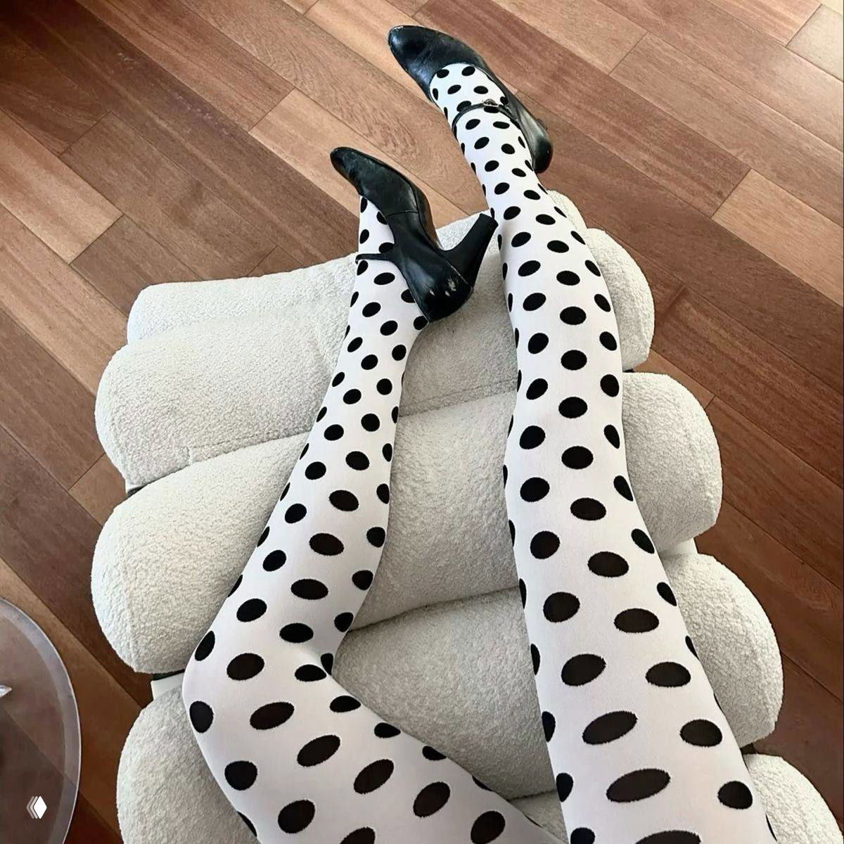 Крупный план: белые колготки в крупный чёрный горох на фоне мягкого кресла и деревянного пола с акцентом на графичный принт и фактуру.