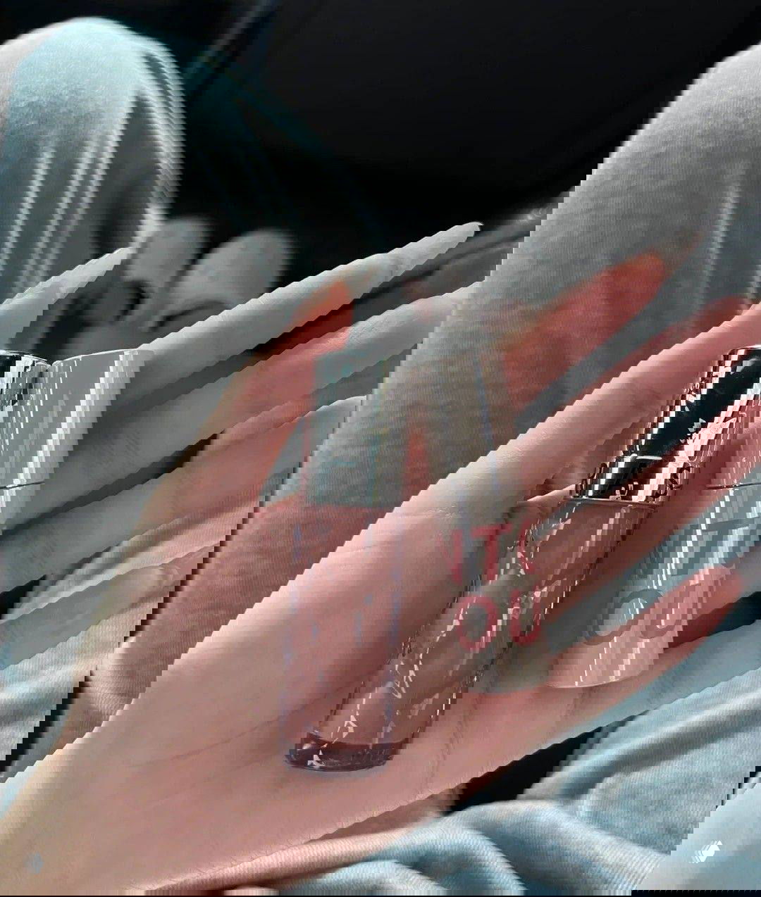 Крупный план руки с аккуратными ногтями, держащей два косметических продукта в нюдовых оттенках — блеск и стиковую помаду на повседневном фоне