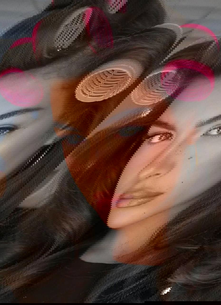 Портретная съёмка женщины в больших розовых бигуди, мягкий контуринг, румянец и нюдовые губы — образ в ретро‑стилизации с естественной текстурой кожи