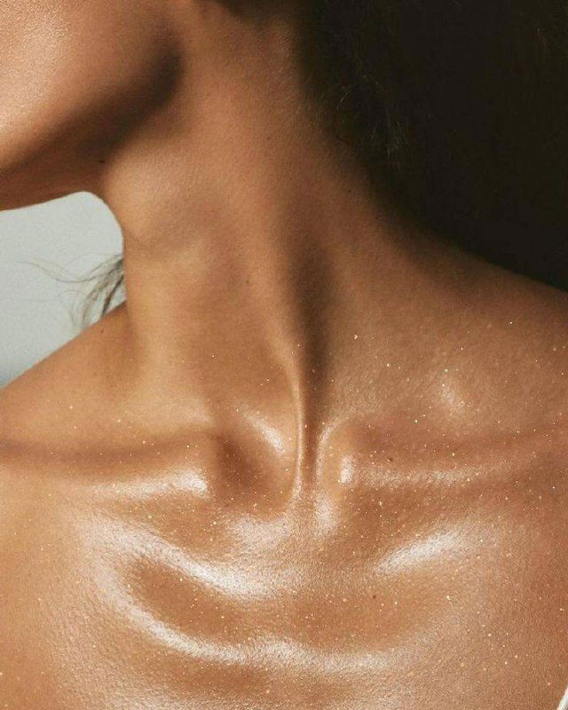 Профиль шеи и ключицы с перламутровым шиммером, бронзовый оттенок и отражения света подчёркивают контуры тела в эстетичной съёмке.