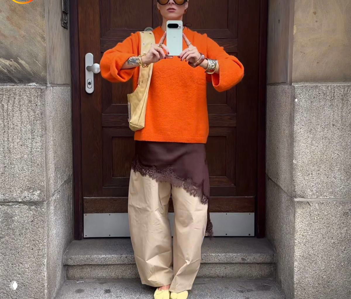 Образ в дверном проёме: женщина делает селфи в ярком оранжевом свитере с многослойными элементами и широкими брюками — пример сочетания цвета и фактур.