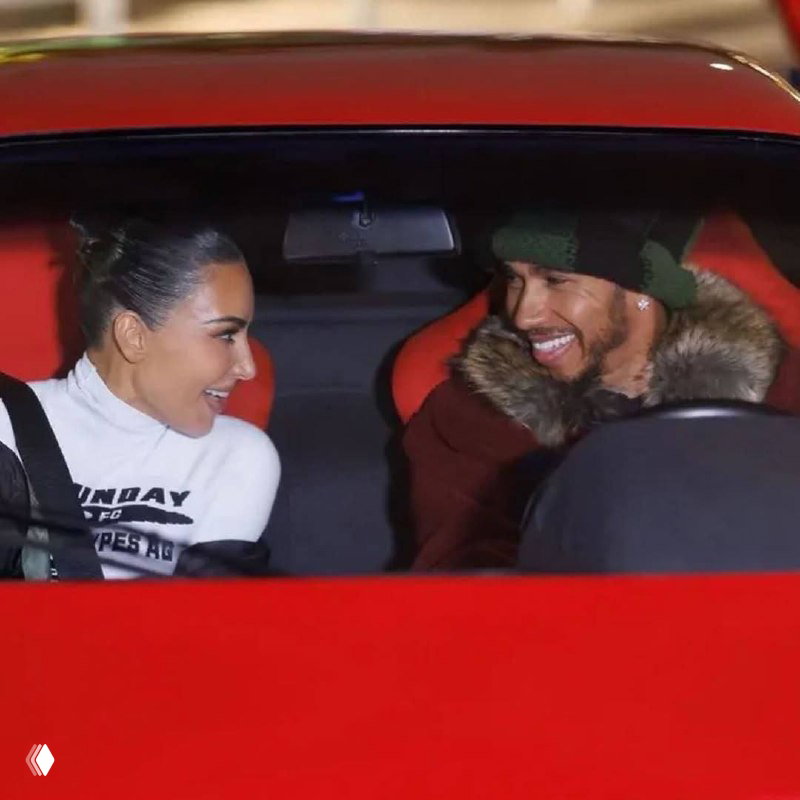 Два человека в салоне красного спортивного автомобиля улыбаются и смотрят друг на друга, интерьер с яркими красными креслами и тёплая ночная атмосфера.