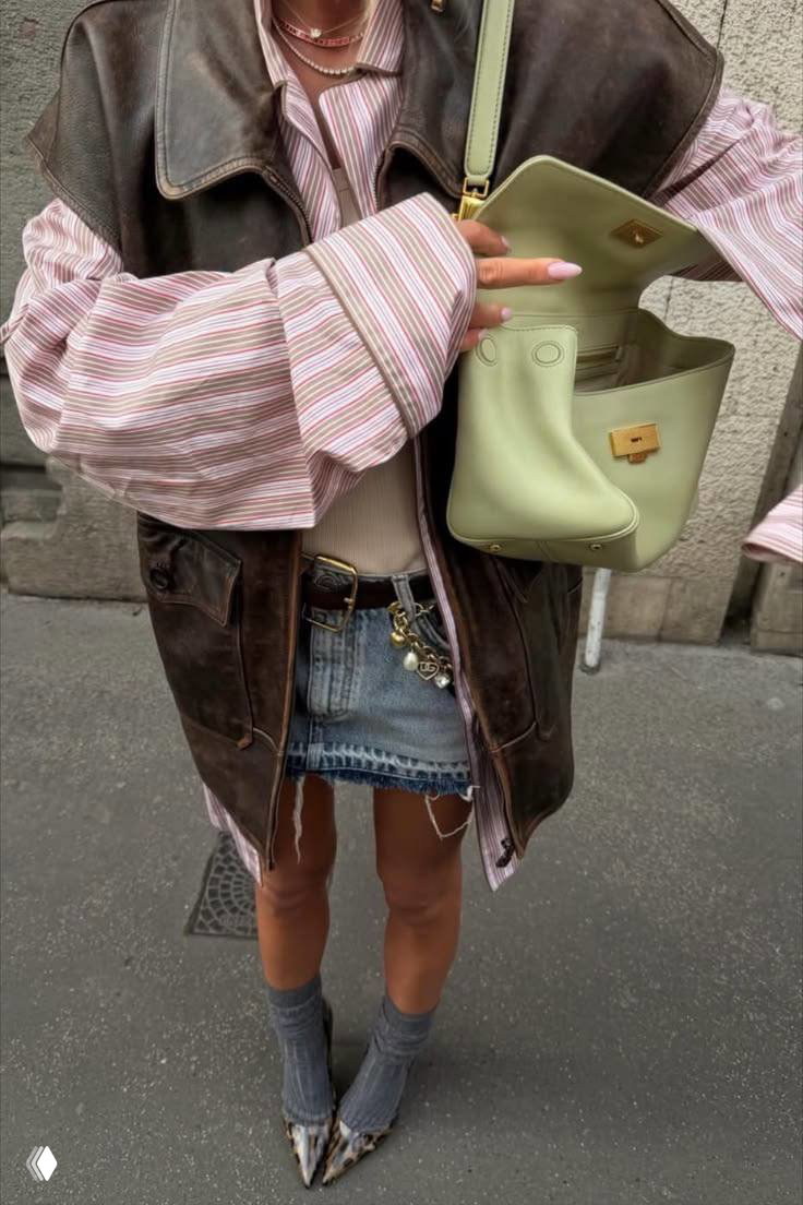 Фрагмент образа: джинсовая мини-юбка в сочетании с полосатой рубашкой, коричневым кожаным жилетом и светло‑зеленой сумкой.