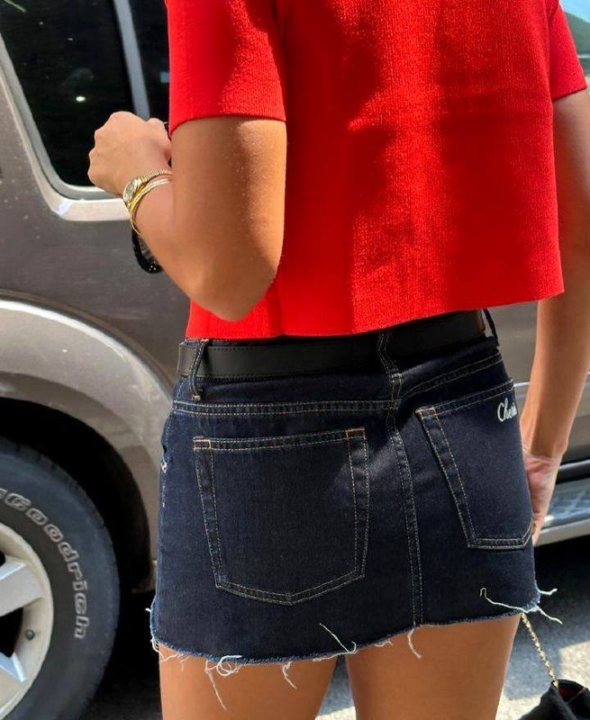 Вид сзади: тёмно-синяя джинсовая мини-юбка с необработанным краем на фоне автомобиля, короткий красный топ и аксессуары.
