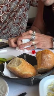Руки мужчины в крупных кольцах и браслетах рядом с тарелкой и кусочками хлеба на столе — превью кадра из видео с Эмиром Текином за трапезой.