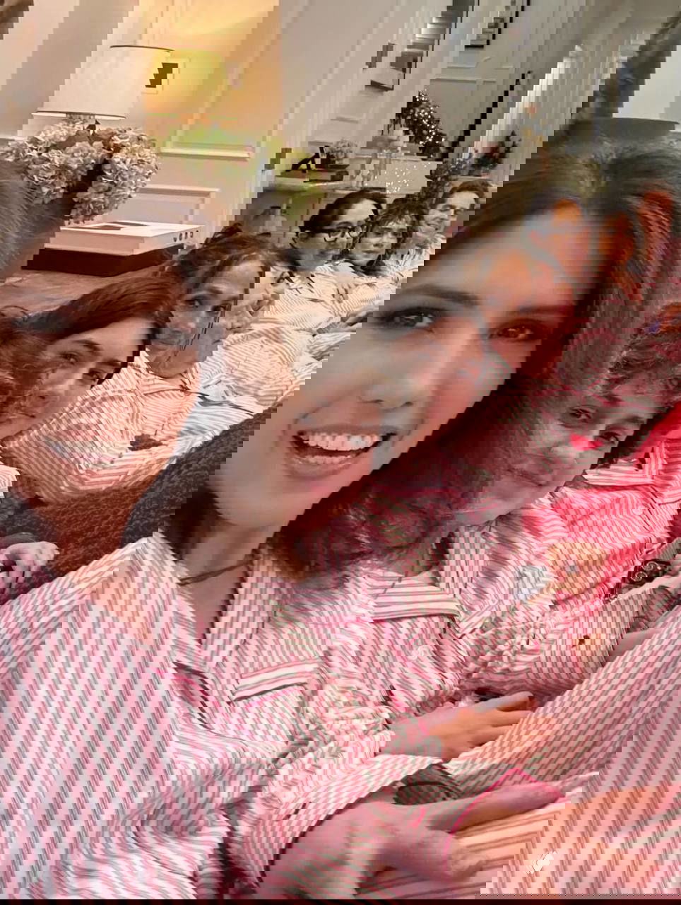 Несколько членов семьи улыбаются в одинаковых розовых полосатых пижамах, они сидят вплотную на диване в украшенной гирляндами гостиной.