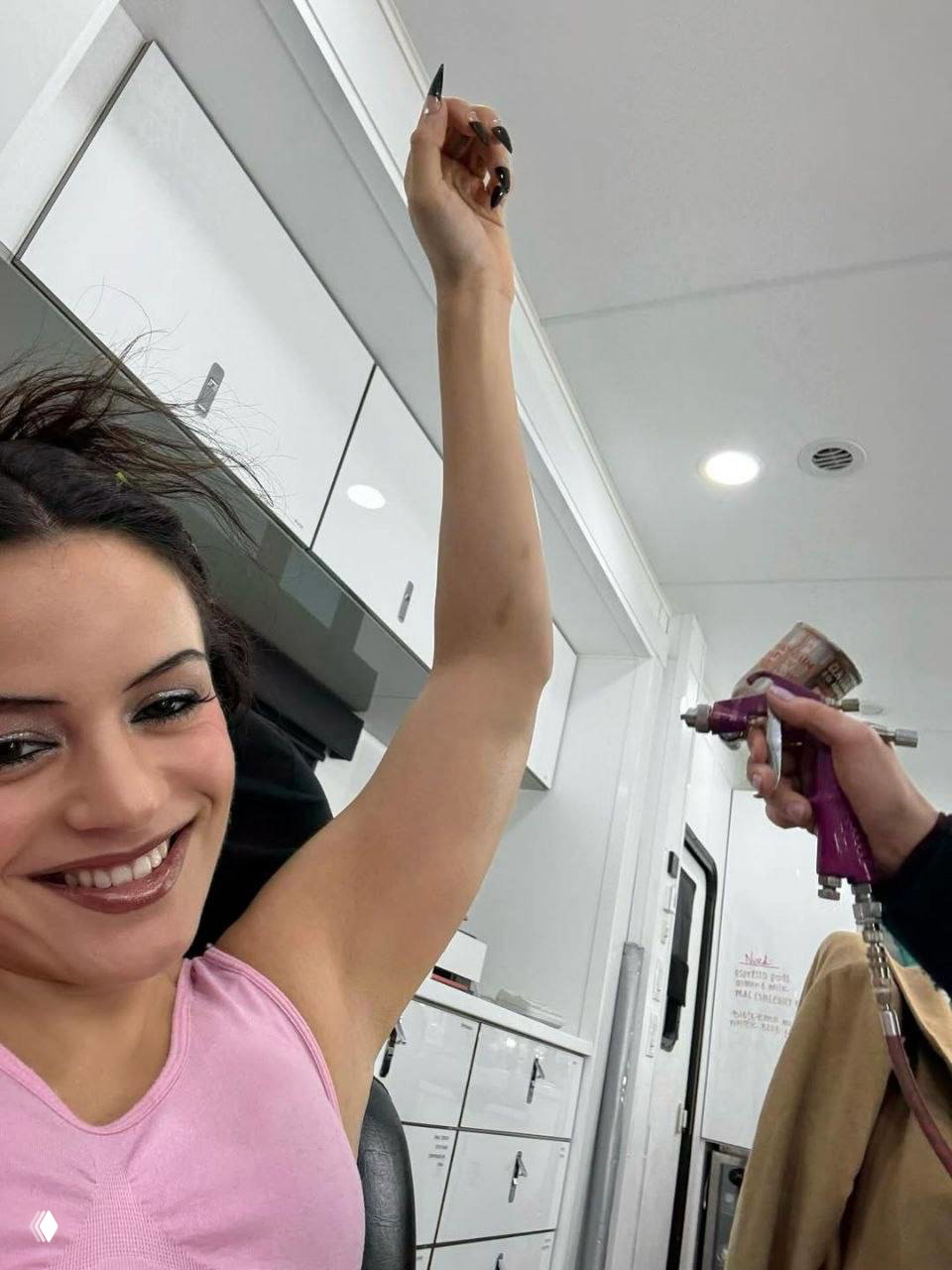 Самофото актрисы в гриме в трейлере гримёрки: поднятая рука и процесс нанесения бронзатора или автозагара, закулисная атмосфера