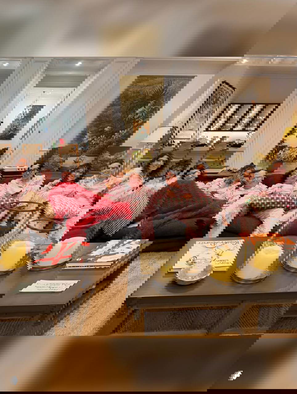 Широкий семейный кадр: несколько человек в одинаковых розовых пижамах лежат и сидят на диване в гостиной, перед ними журнальные столики и свечи.