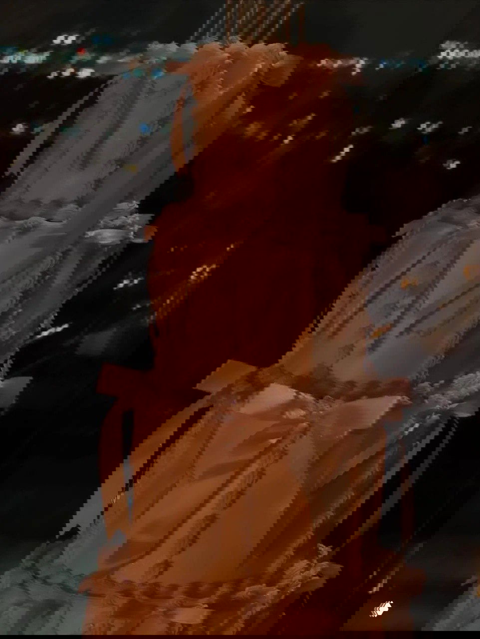 Трехъярусный кремовый праздничный торт с бантами и рюшами на фоне вечернего города: элемент мини-вечеринки в честь дня рождения.