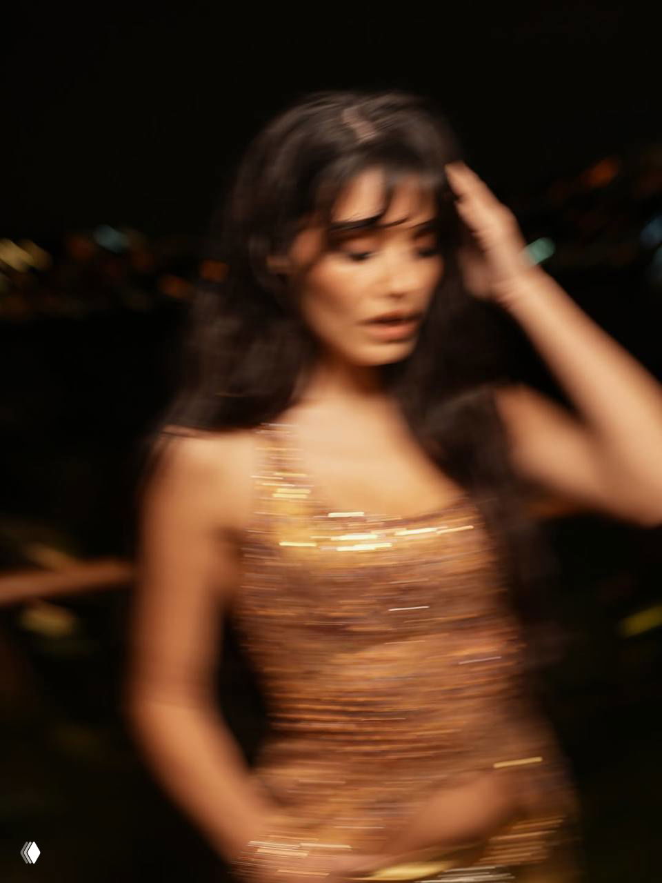 Размытый динамичный портрет в золотистом наряде, движение волос и блеск ткани на фоне мерцающих огней ночного города.