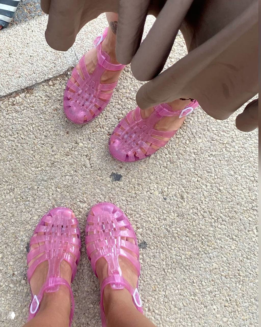 Две пары прозрачных розовых jelly shoes на гравийной дорожке, вид снизу подчёркивает переплётённую структуру и застёжки из ПВХ на обуви.