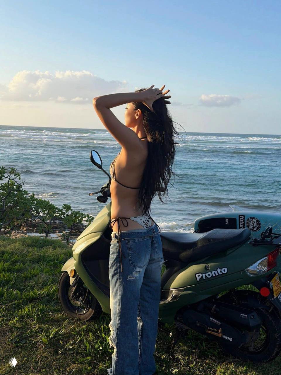 Профильная фотография модели у моря в бикини и джинсах, руки подняты — кадр на закате из промосъёмки пляжной коллекции.