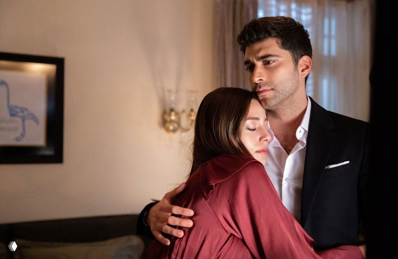 Кадр из домашней сцены: мужчина обнимает женщину, она закрыла глаза — интимный момент между персонажами в интерьере.