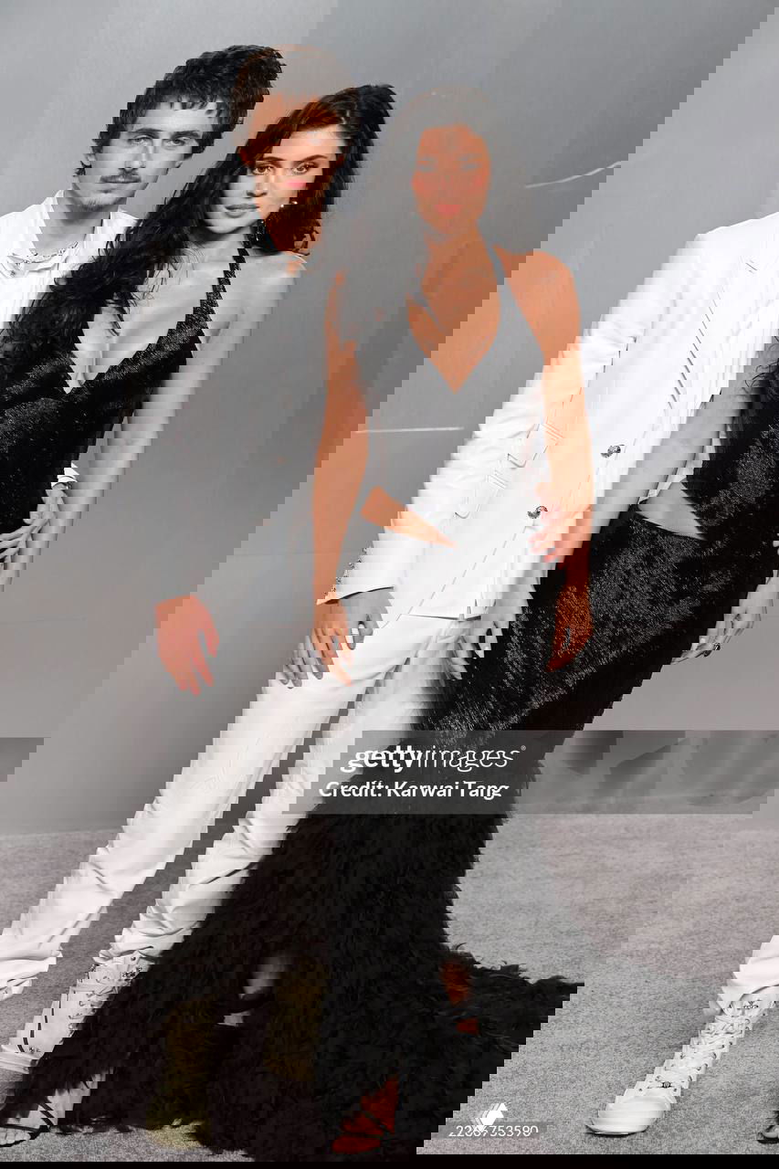 Дуэт на красной дорожке: мужчина в светлом костюме и женщина в глянцевом чёрном платье с разрезом и длинным хвостом на полу.