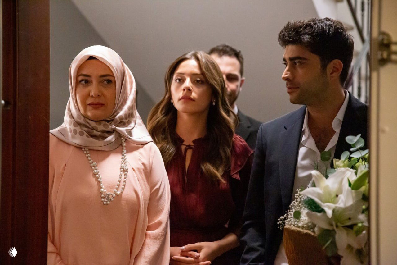 Группа персонажей у дверей квартиры: женщина в платке, другая женщина и мужчина с букетом — сценическая постановка у порога.