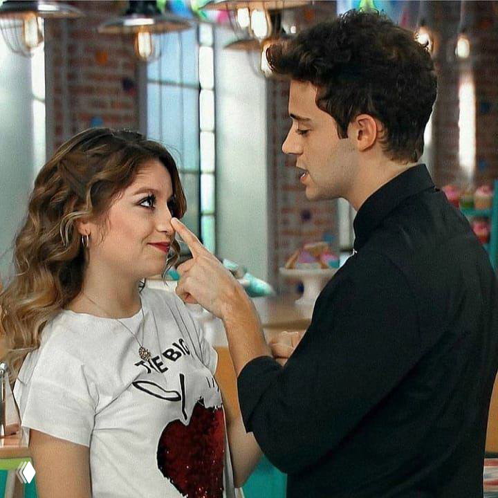 Кадр из «Soy Luna»: Амбар и Симон в игривом моменте — он касается её носа; интерьер студии и цветное освещение вокруг персонажей.