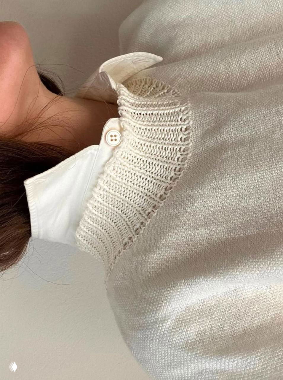 Крупный план светлого образа: вязанный воротник и белая рубашка на шее модели — нежные кремово‑белые текстуры одежды в оттенке Cloud Dancer.