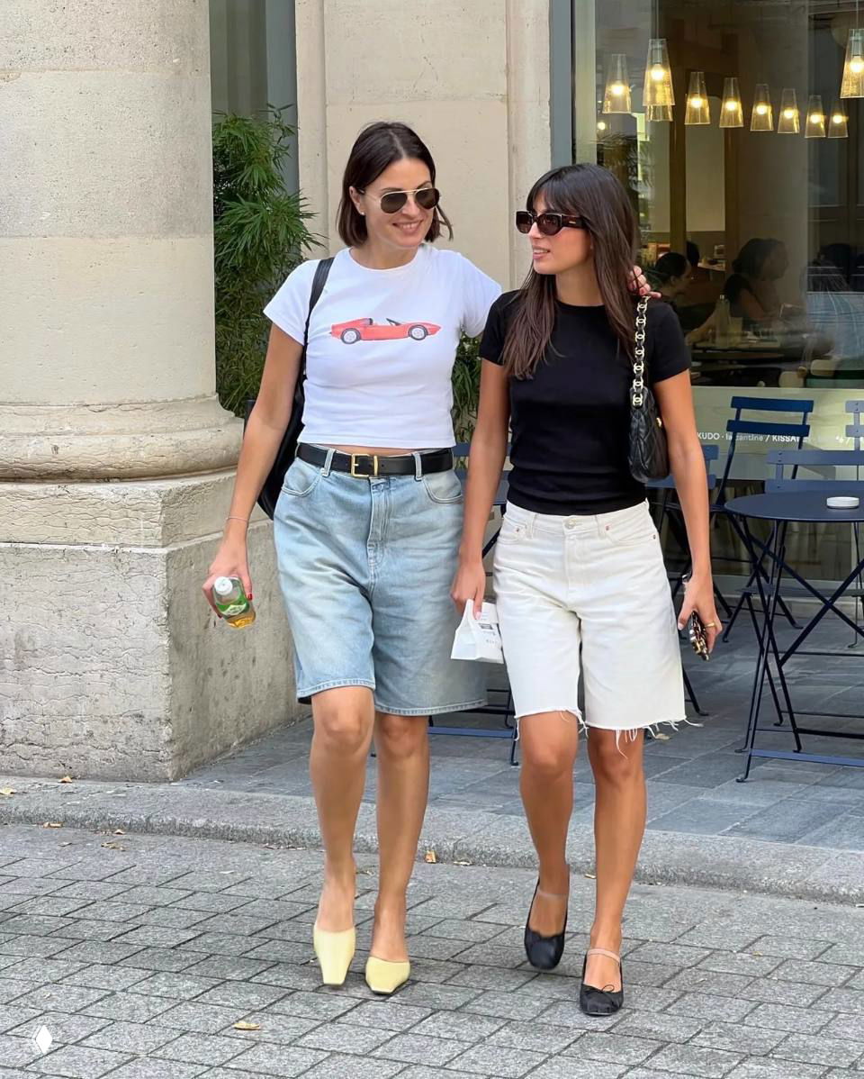 Две женщины в джинсовых и светлых бермудах идут по улице в футболках и туфлях, непринуждённый повседневный городской образ для прогулки