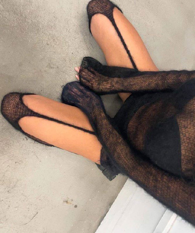 Кадр сверху на ноги и образ в полупрозрачной тёмной вязаной ткани: внимание на фактуру материала, силуэт и контраст кожи с одеждой в студийной обстановке.