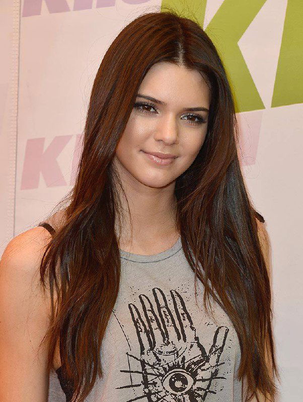 Фотография молодой женщины в повседневном образе с длинными тёмными волосами и лёгким макияжем, мягкое интерьерное освещение, улыбка в кадре.