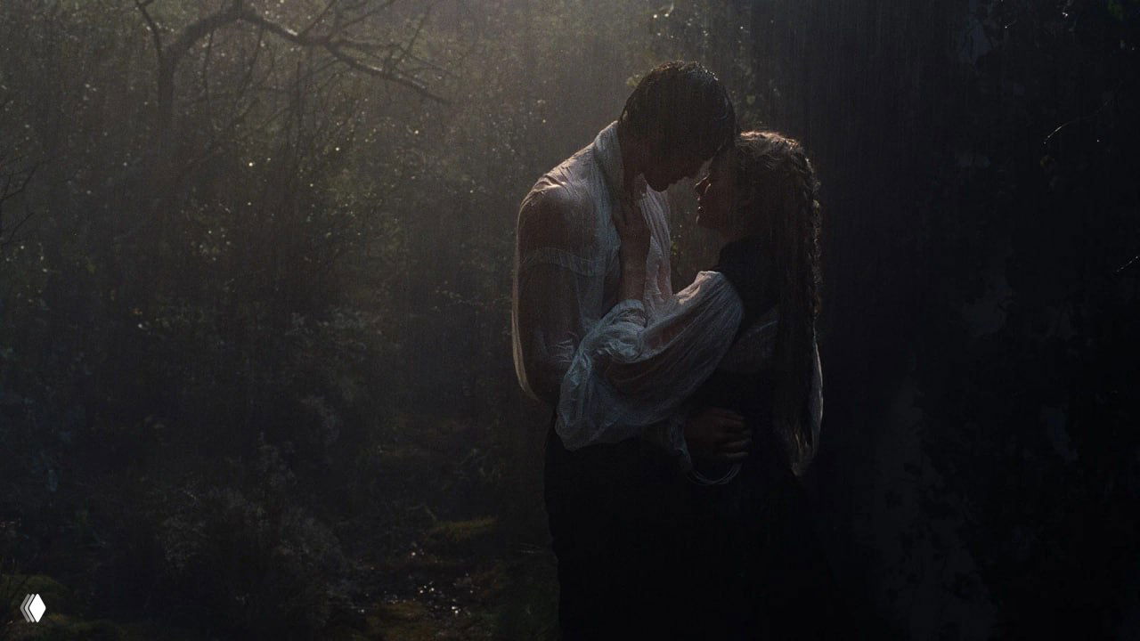 Интимная тёмная сцена с Джейкобом Элорди и Марго Робби под дождём в лесу, герои в объятиях — кадр подчёркивает плотскую и эмоциональную составляющую фильма.