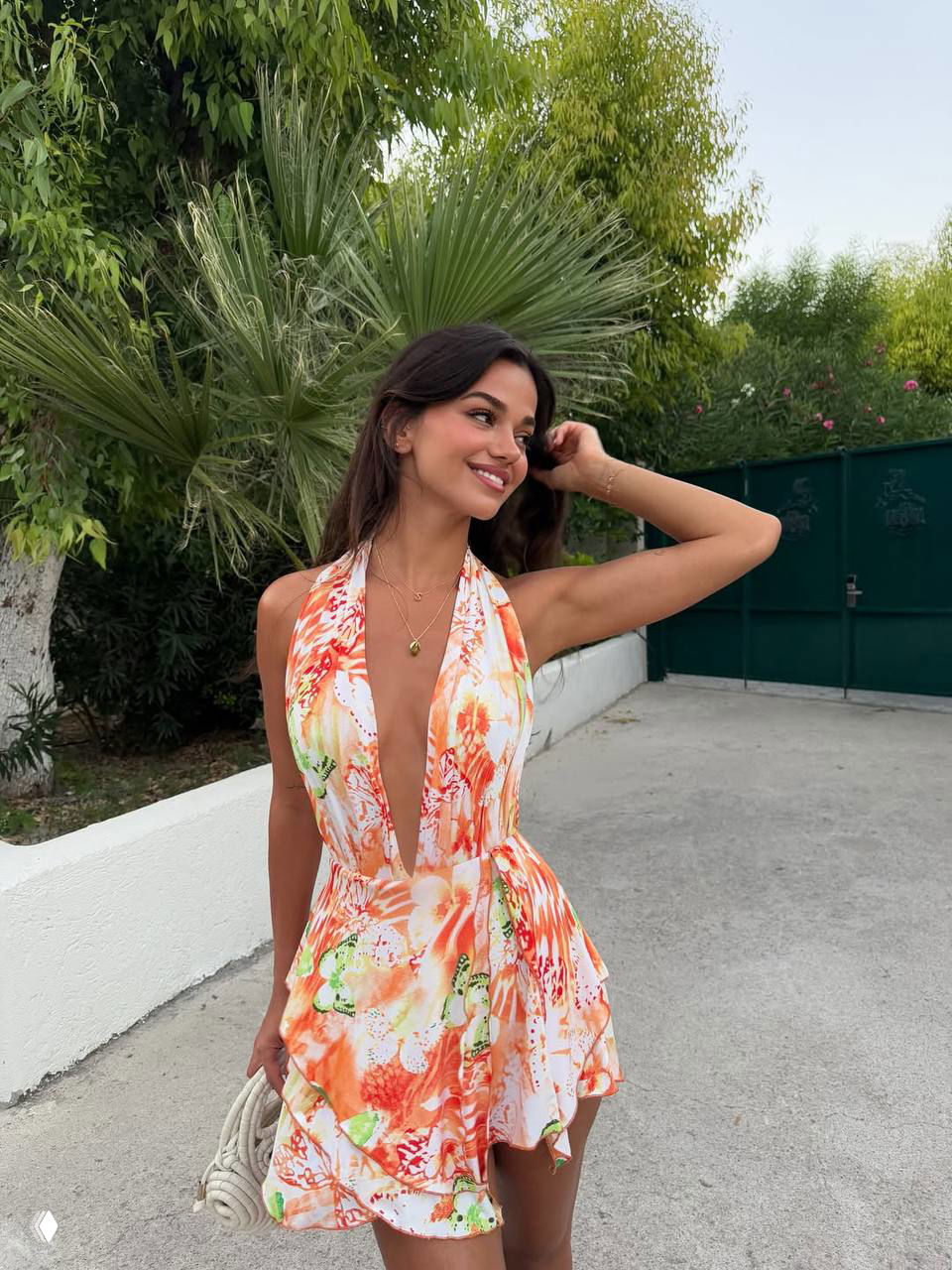 Фото на фоне зелени: улыбающаяся девушка в ярком летнем платье с глубоким декольте и расклёшенной юбкой позирует на открытом воздухе.