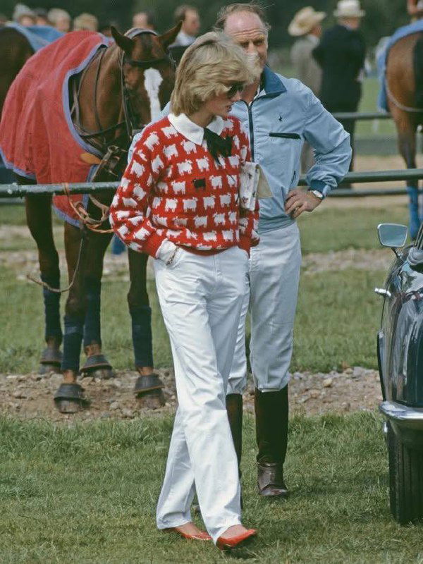 Архивное фото: женщина в красном свитере с белым узором овечек и белыми брюками на фоне поля и лошадей — ретро-образ для вдохновения.