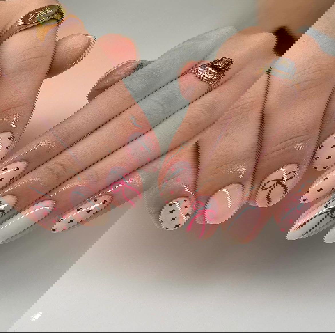 Пара рук с аккуратными овальными ногтями на нюдовой базе, красные тонкие банты и красные точки по всей поверхности, студийный свет отражается в лаке.