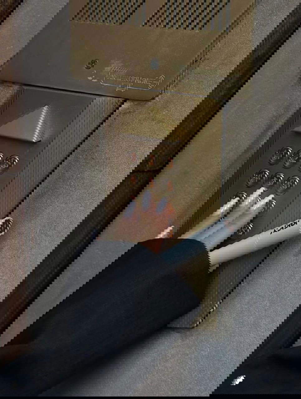 Рука с аккуратным маникюром нажимает кнопку домофона; в руке также белый предмет с надписью REY — деталь повседневной эстетики.