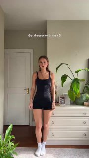 Кадр из видео: блогерка в чёрном мини-платье в домашней обстановке, надпись 'Get dressed with me' на экране — минималистичный весенний вечерний лук.