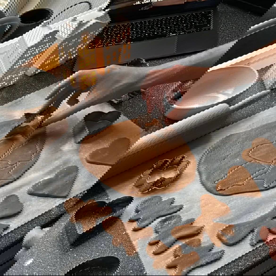 Руки вырезают формочками имбирные фигурки из теста: скалка, формочки звёзд и сердечек, рабочая поверхность с тестом и праздничными аксессуарами.