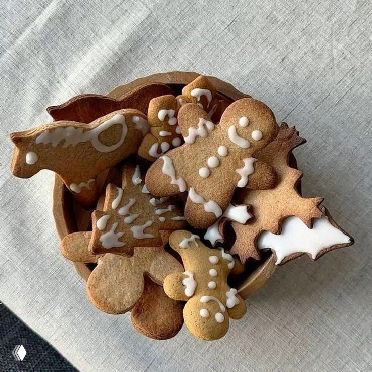 Миска, наполненная имбирными пряниками разных форм, украшенными белой глазурью; тёплая подача на текстильной поверхности, натюрморт для уютного настроения.