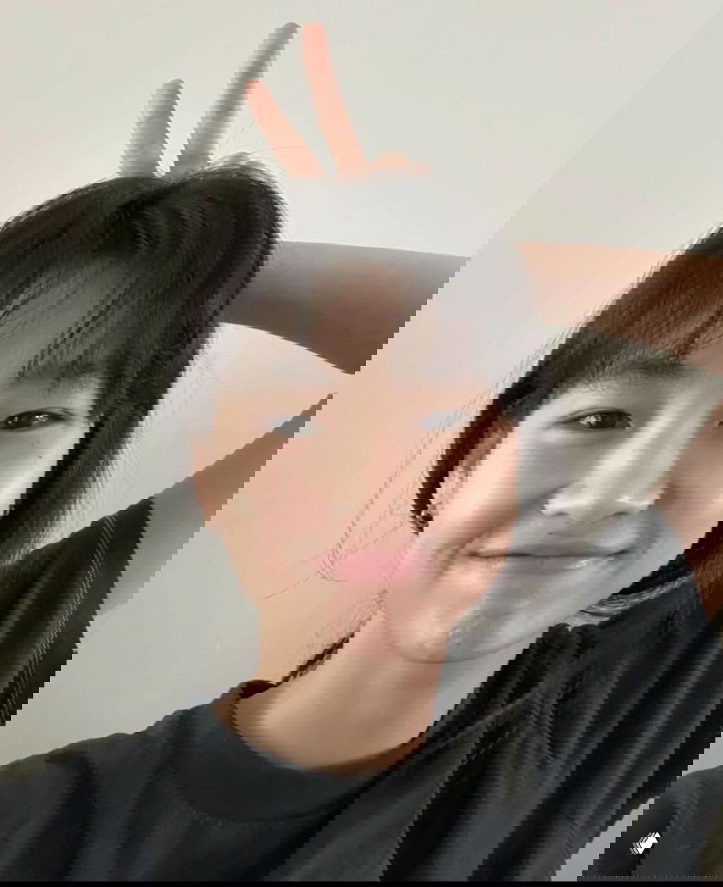 Селфи улыбающейся молодой женщины в тёмной футболке на простом фоне; натуральный вид, видна кожа без плотного макияжа.