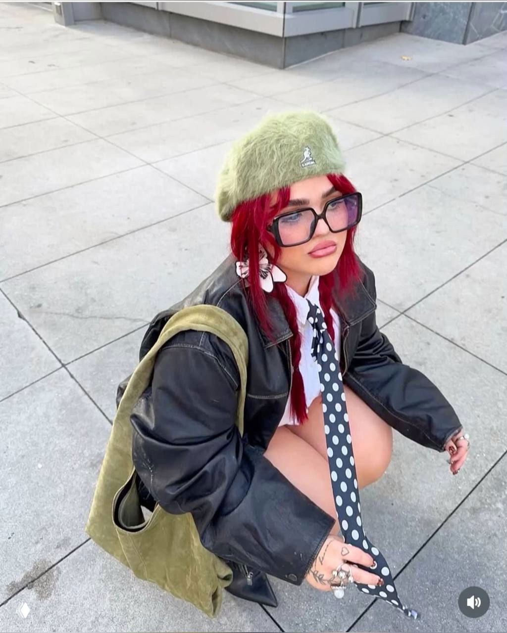 Уличный кадр: яркая девушка с красными волосами и крупными тёмными очками в бретоновском стиле — лук в духе городского ретро и неформальной эстетики.