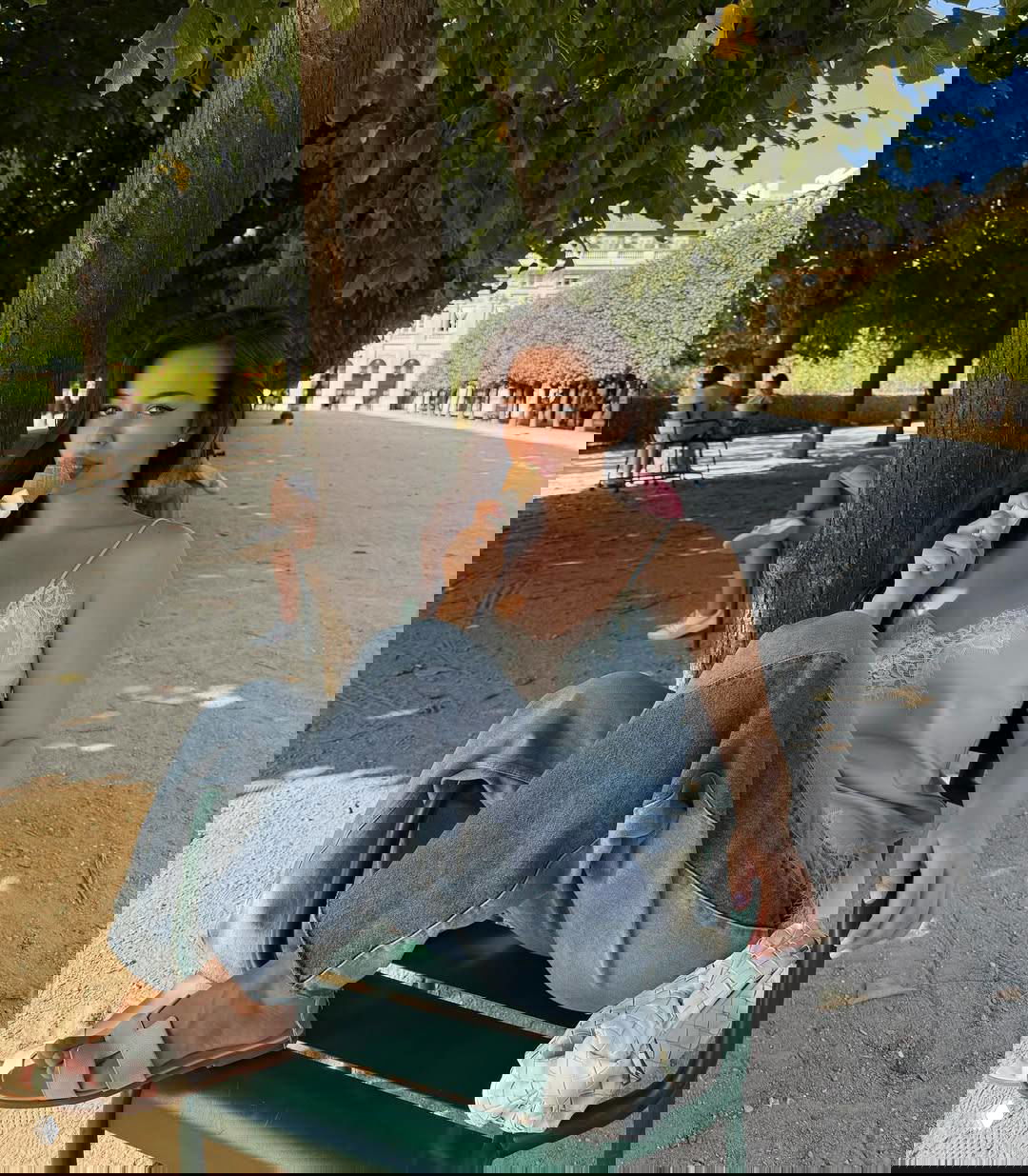 Девушка невысокого роста сидит в парке под деревом с мороженым, в лёгком топе и джинсах — пример спокойного летнего casual‑лука для миниатюрных девушек.