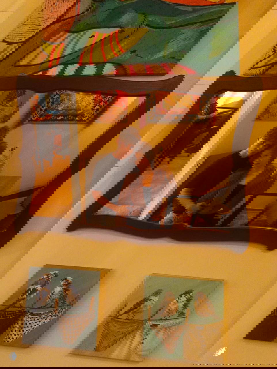 Отражение пары в настенном зеркале: мужчина обнимает женщину, вокруг видно картины и предметы декора, тёплое домашнее освещение создаёт уютную атмосферу.