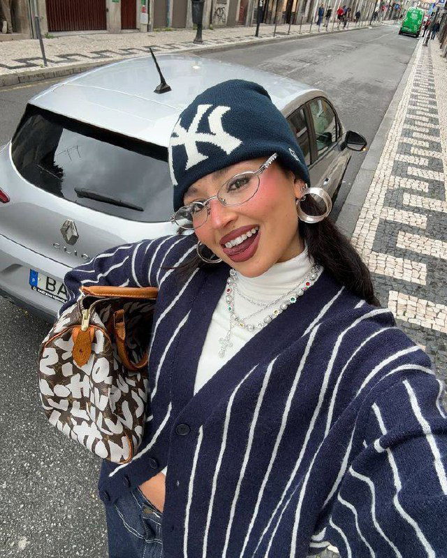 Селфи на улице: девушка в шапке и узких металлических очках-нулёвках улыбается — сочетание спортивного аксессуара и делового стиля.