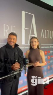 Фото с пресс‑вола: двое людей позируют перед баннером с именем Emre Altug, внизу виден логотип theGirl на мероприятии.