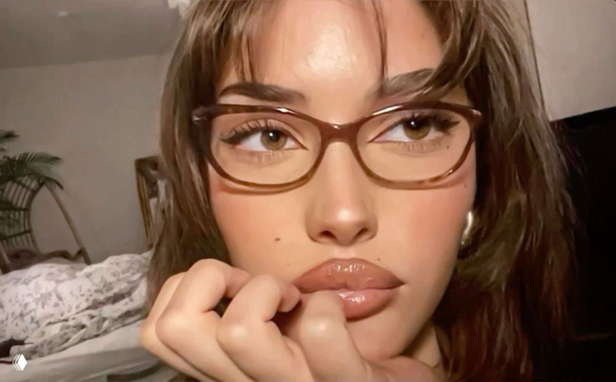 Девушка делает селфи в городском пейзаже в больших квадратных коричневых очках — яркий аксессуар подчёркивает макияж и украшения.