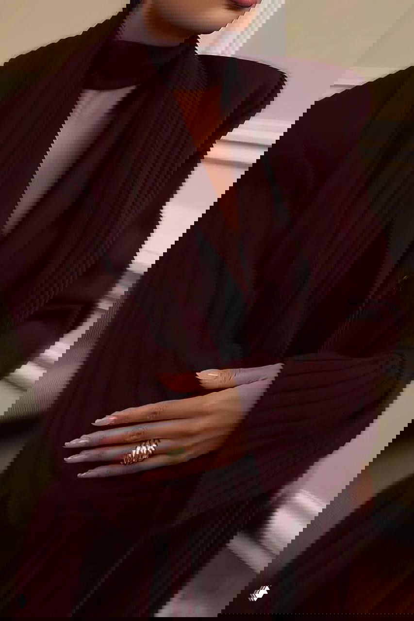 Крупный план бордового костюма с фактурным шарфом и аккуратными руками с украшениями — деликатная комбинация строгих линий и бархатистой текстуры.