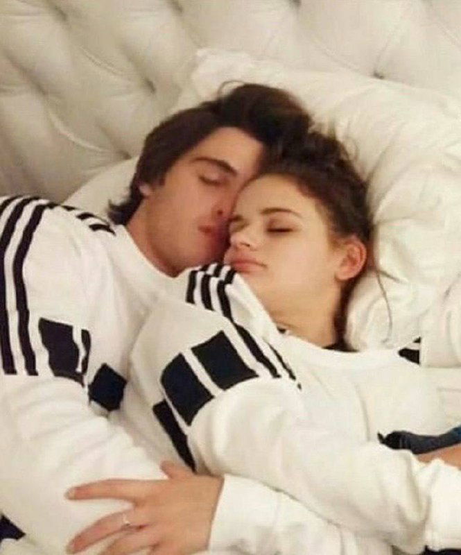 Двое людей лежат в постели, обнимаются и отдыхают; спокойный домашний кадр без откровенного контента.