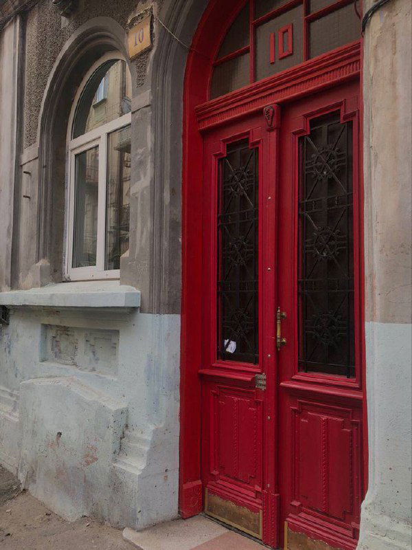 Красная дверь старинного дома на фоне серых фасадов; эстетический кадр с насыщенным алым цветом в городской среде.